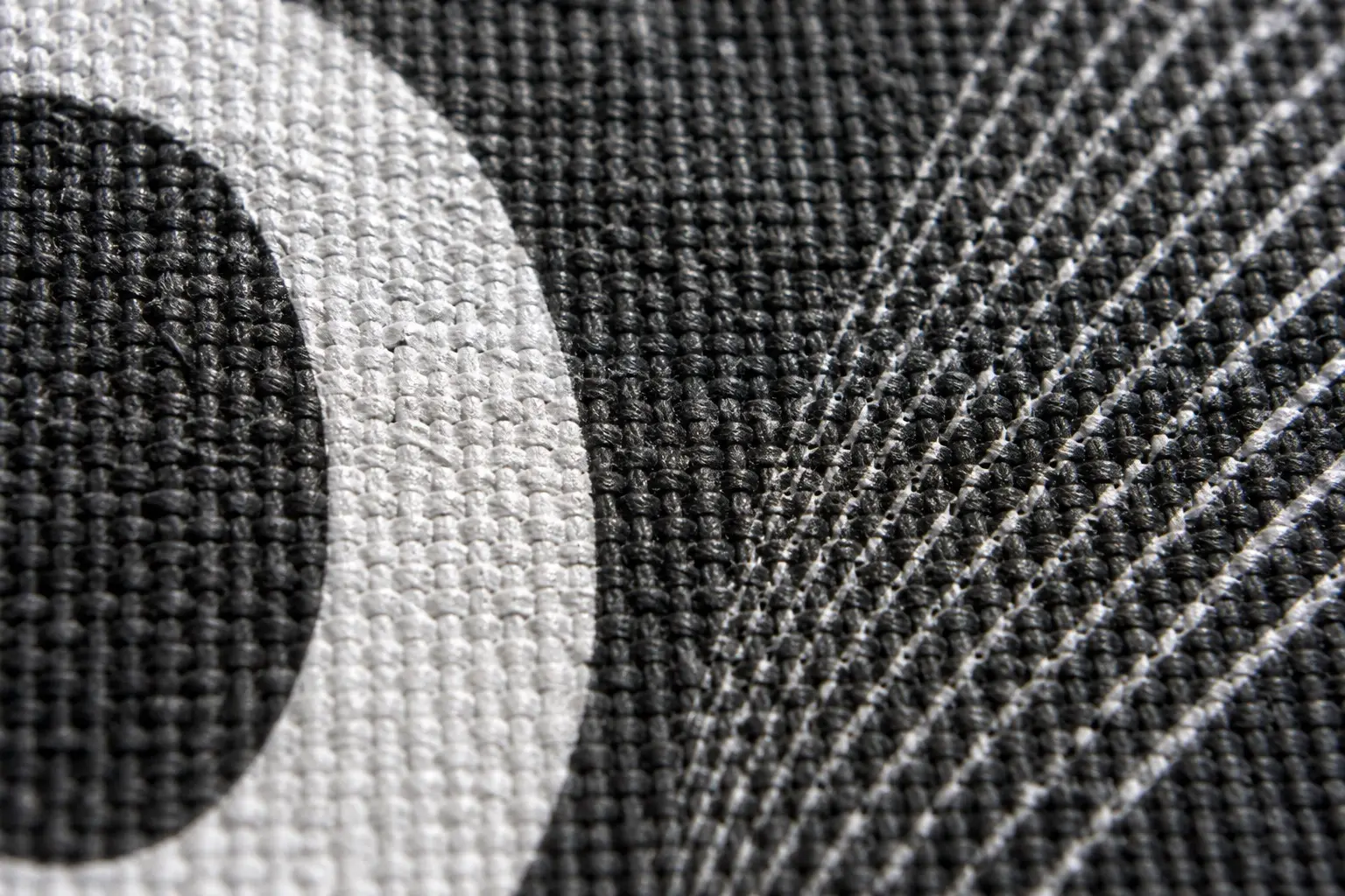 An extreme close-up of a printed dark tee — a bold white curve holding a clean edge while a set of fine hairlines beside it breaks up over the weave