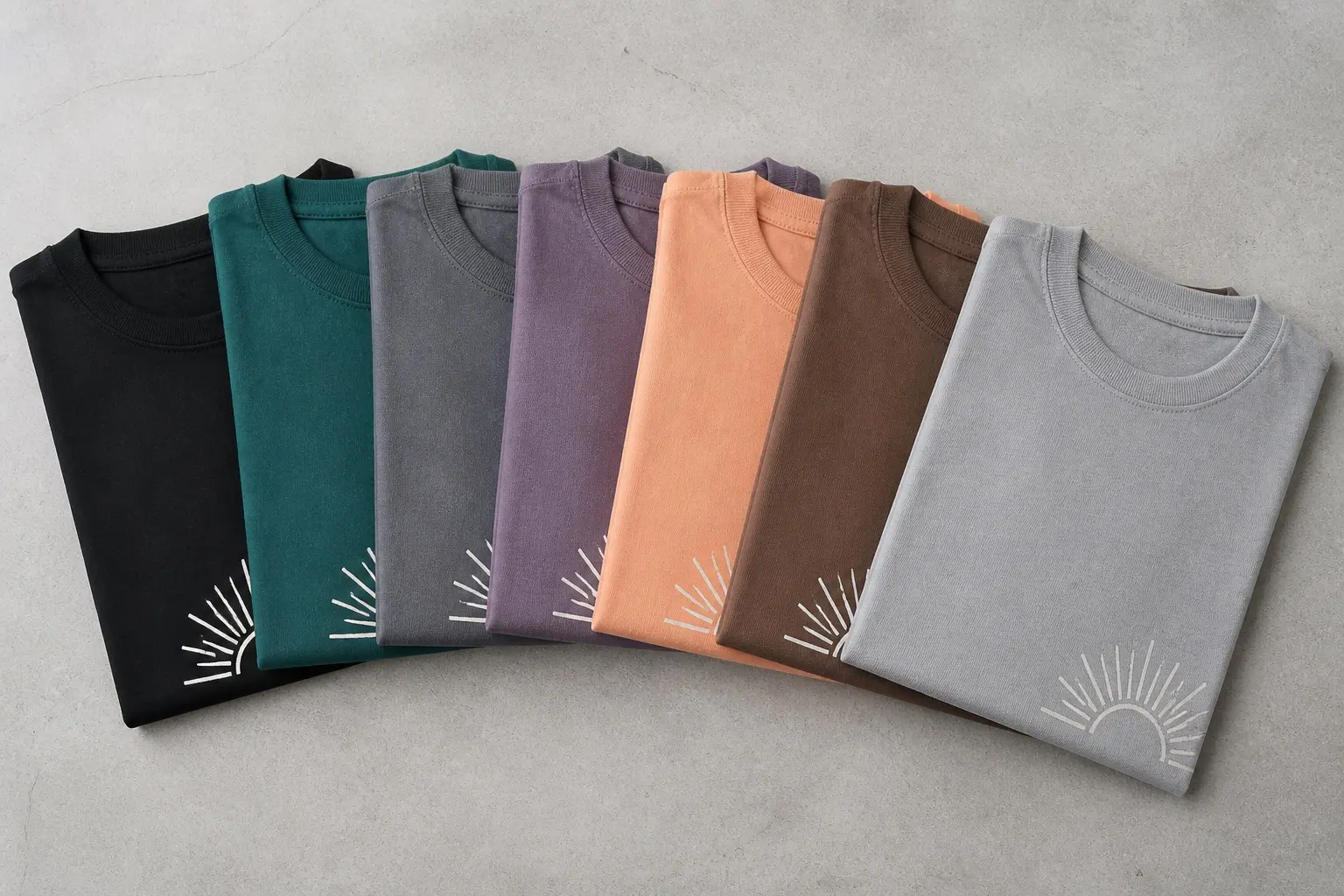 Seven folded tees fanned out in black, teal, grey, purple, peach, brown and pale grey, each printed with the same small white sunburst