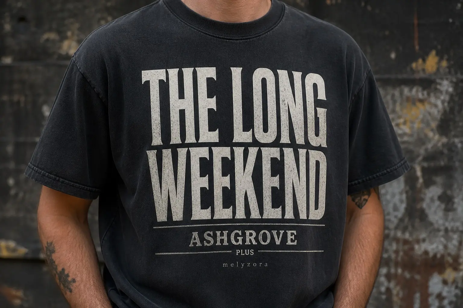 A washed black tee worn from the chest down, printed with a billing block of three band names at sharply descending sizes — THE LONG WEEKEND enormous, ASHGROVE about half that size, and a third name small enough to squint at with PLUS above it in even tinier type, the names separated by thin rules